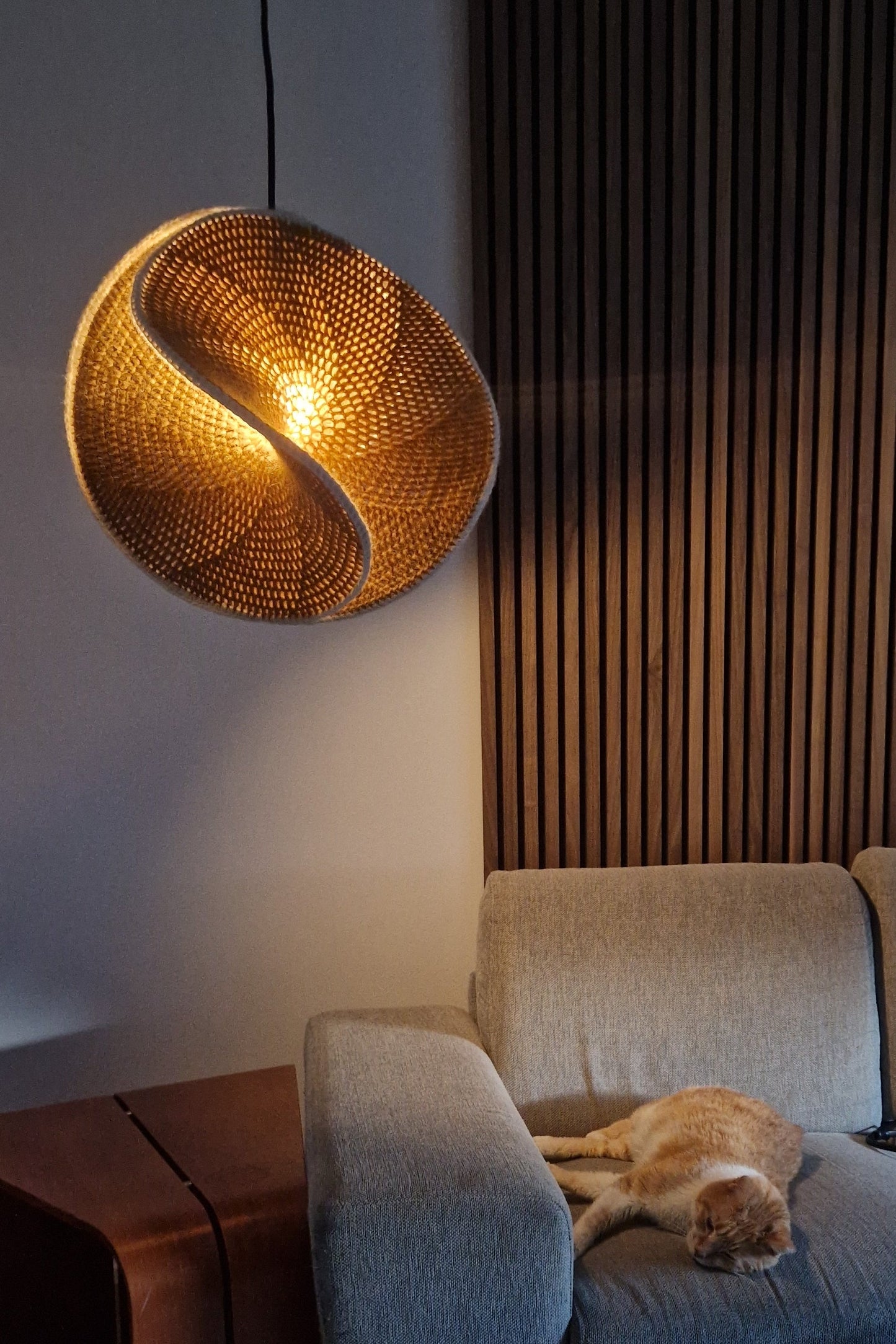 Cat sitting on a textured armchair next to a woven lampshade.